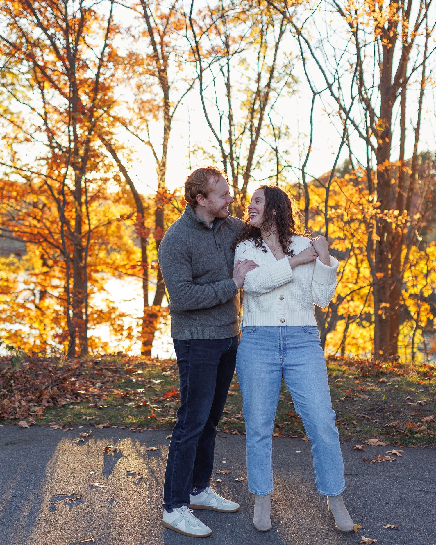 A couple shares a romantic moment at sunset in an autumn forest setting with golden leaves and warm lighting.