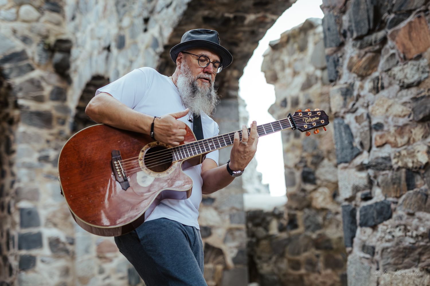 Musicians perform with acoustic guitars against stone wall backdrop.