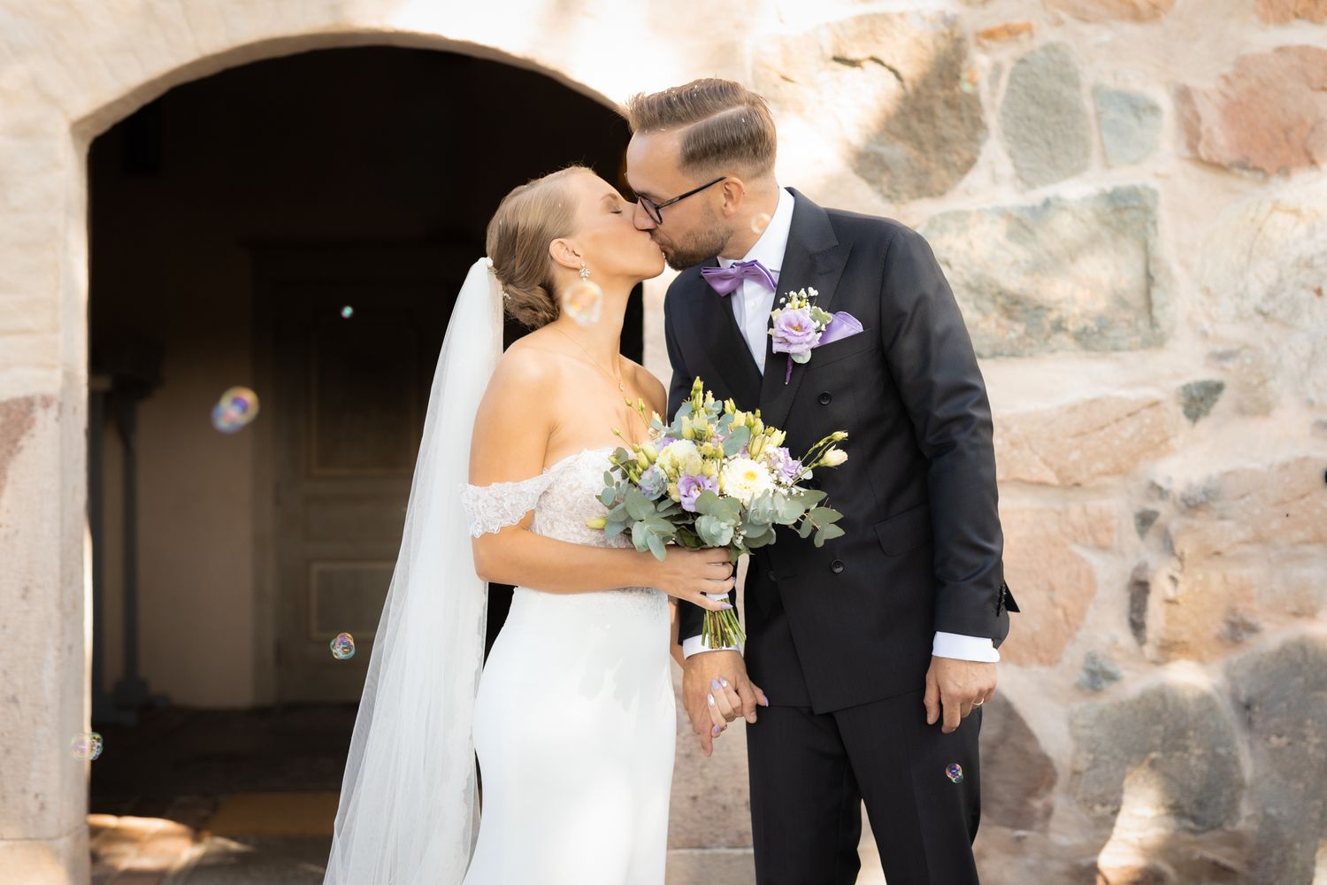 Wedding couple shares intimate moment against rustic stone wall backdrop.