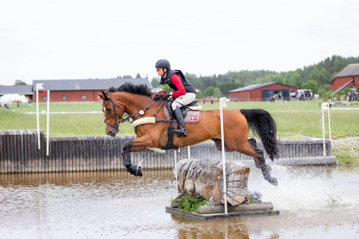 Multiple horses and riders navigate water obstacles during cross-country competition.