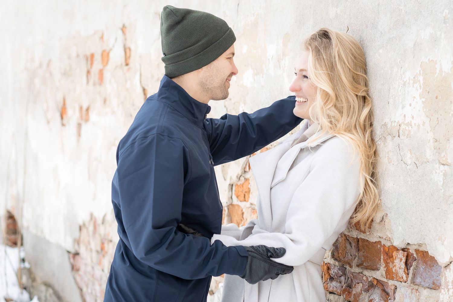 Couple poses together against rustic white wall during romantic photoshoot.