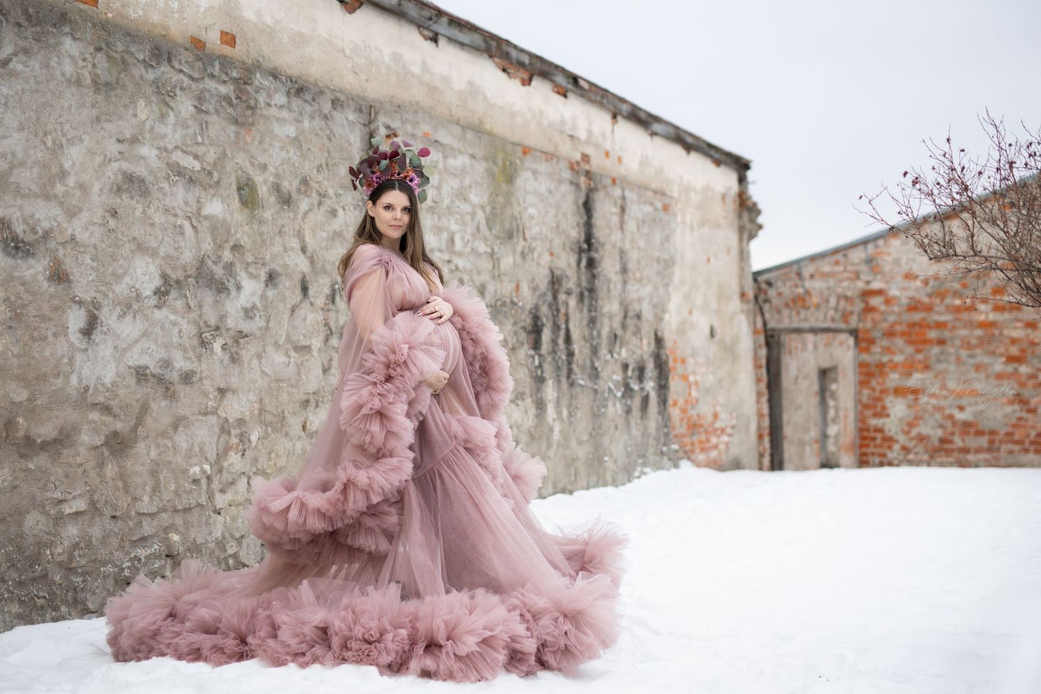 A flowing pink tulle gown creates a dreamy silhouette against weathered stone walls and snowy ground.