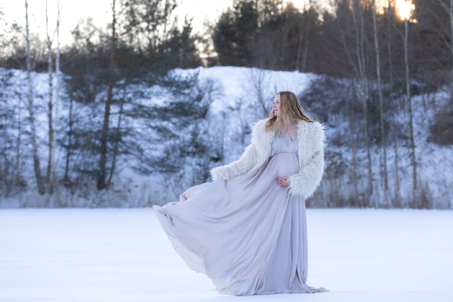 Ethereal winter photography with flowing white dress against snowy forest backdrop.