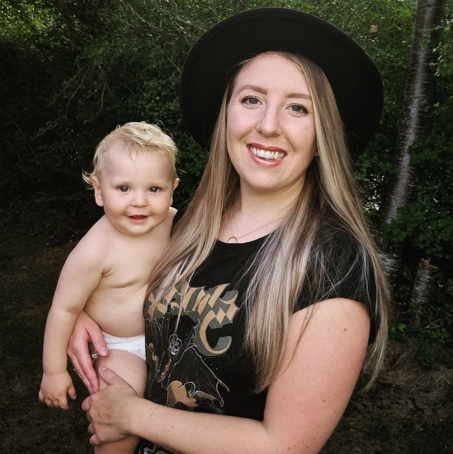 Mother and baby portrait session in wooded setting with black hat.