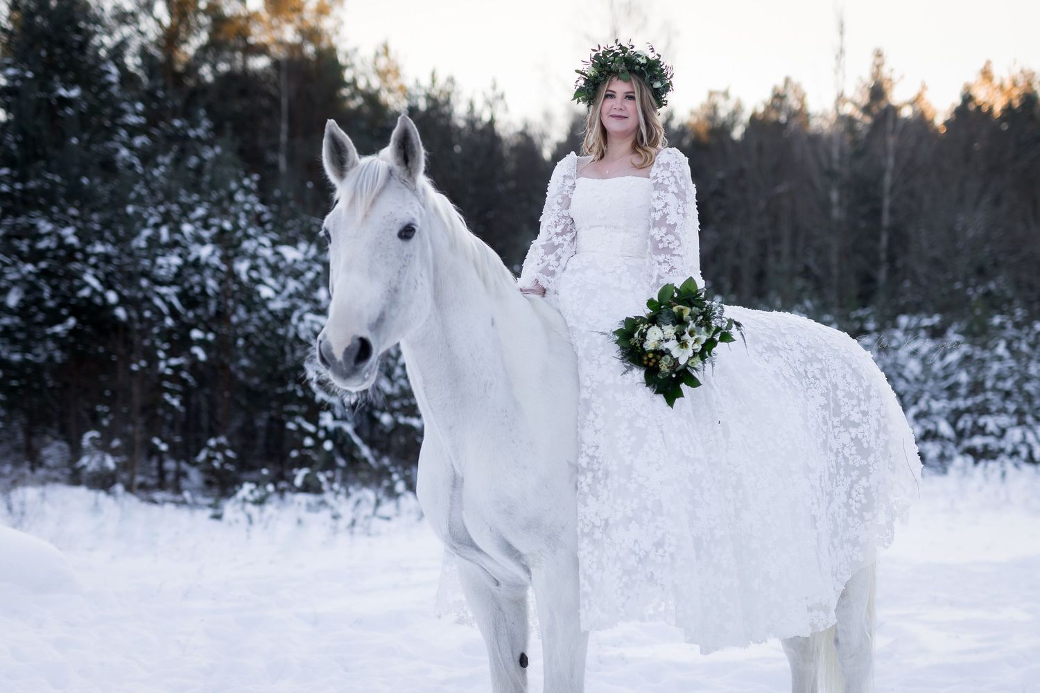 Magical winter bridal shoot with white horses in a snow-covered forest setting.