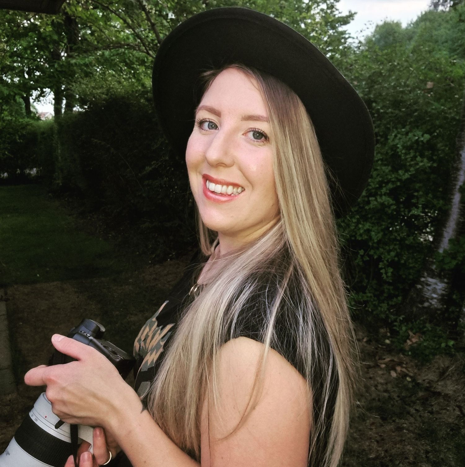 Stylish portrait session in black hat against green forest background.