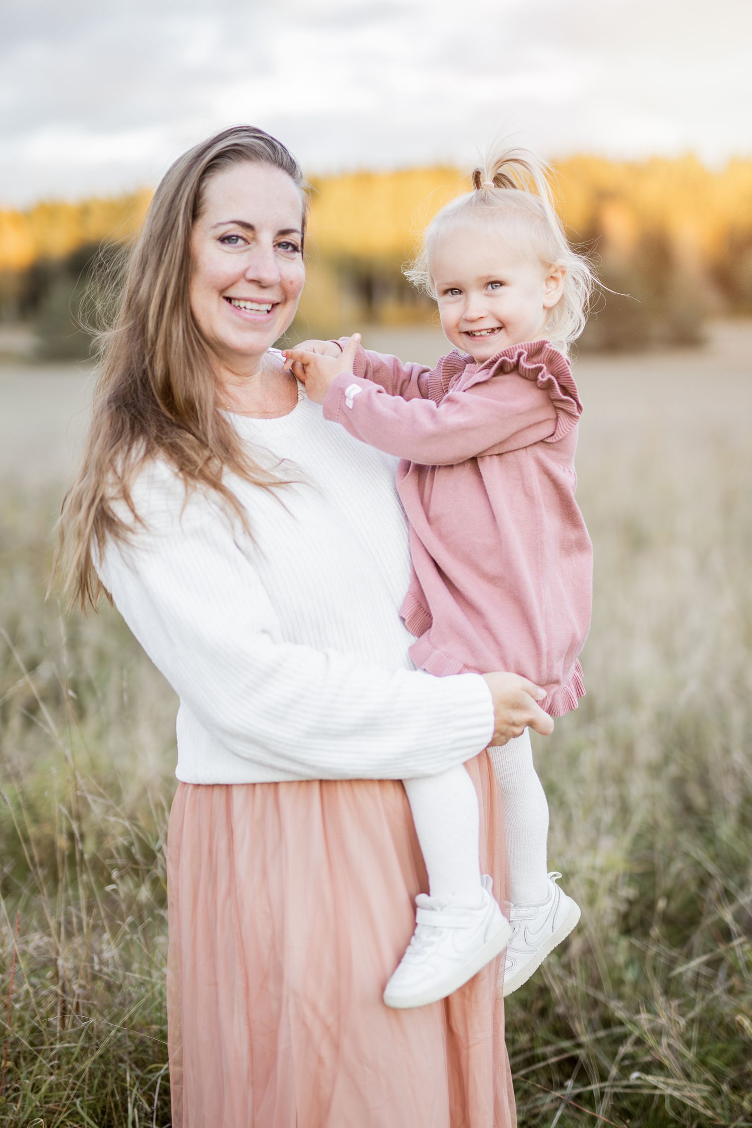 A parent and child share joyful moments in a field at sunset wearing coordinated pink and white outfits.