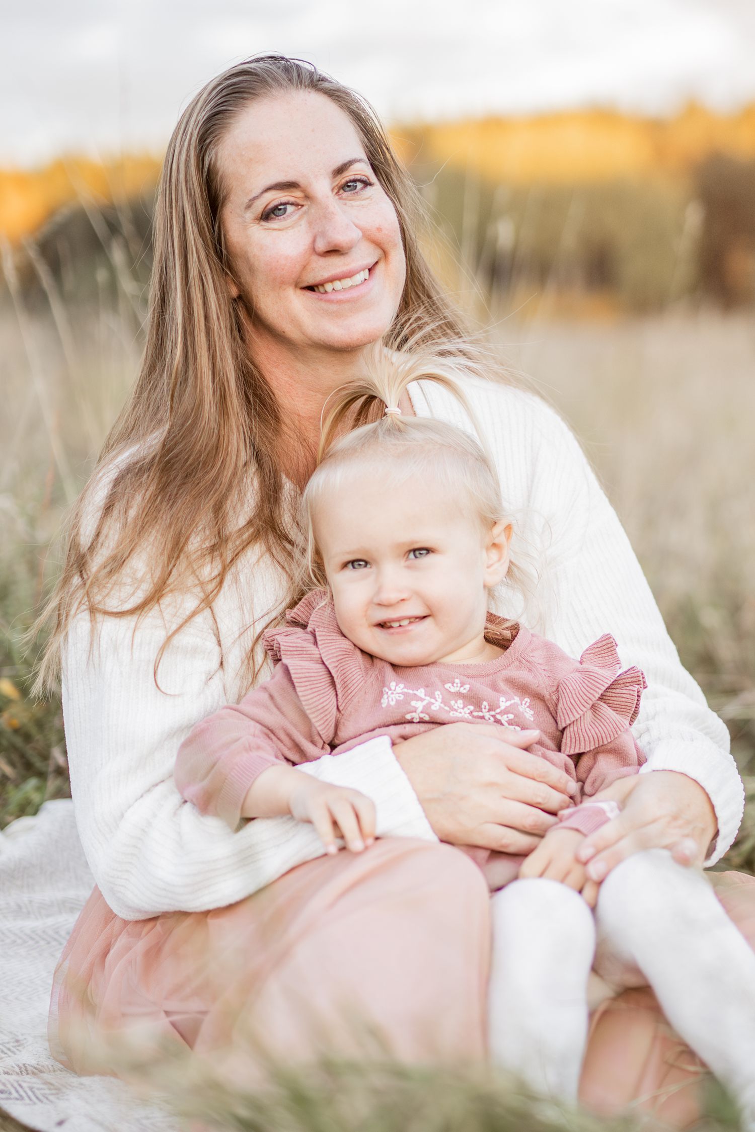 Mother and child share tender moments in a sunlit field wearing white and pink outfits.