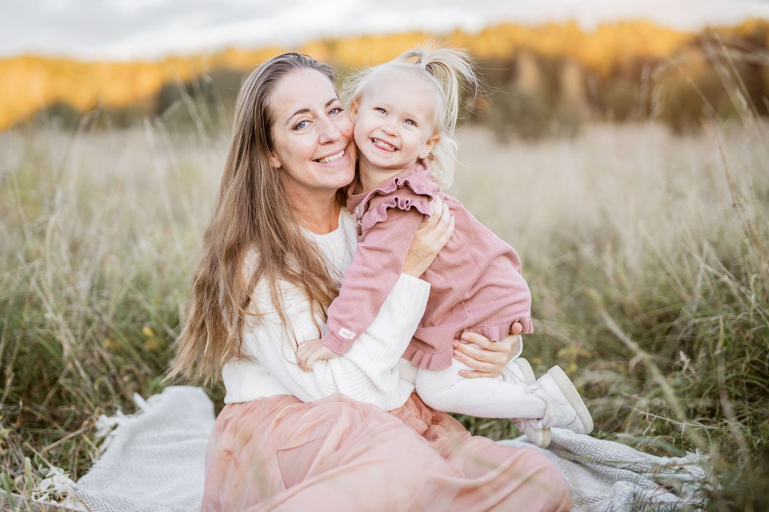 Mother and child share tender moments in a golden field at sunset wearing pink and white outfits.
