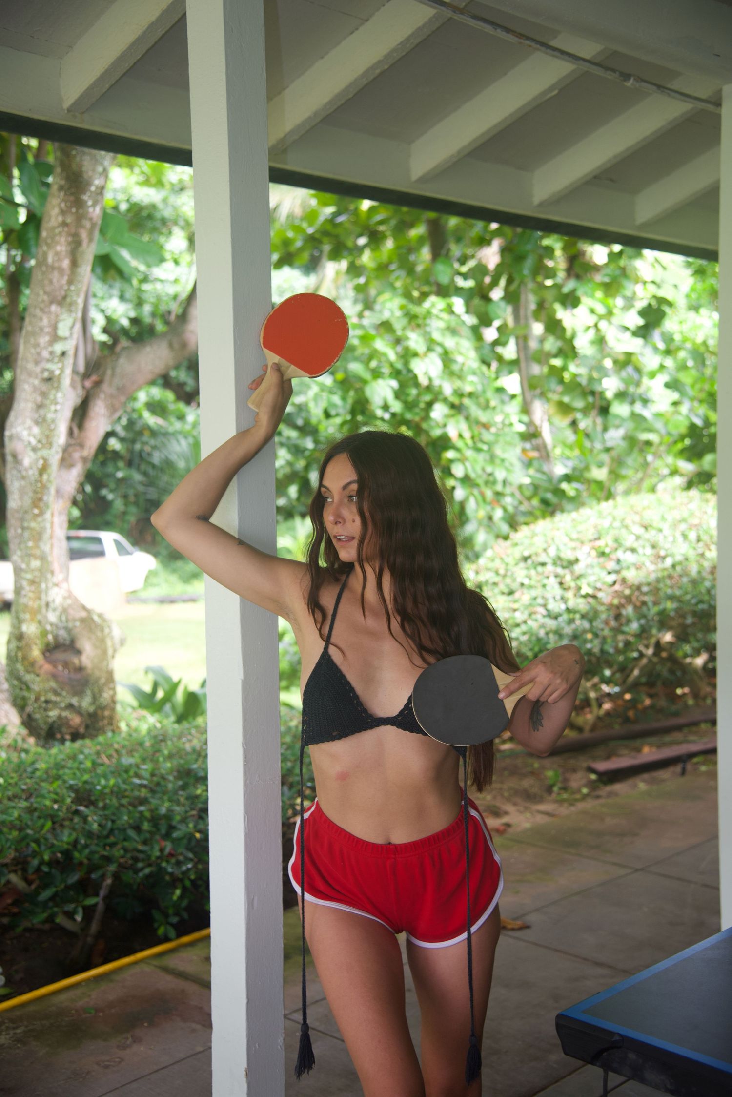 Person playing ping pong on an outdoor covered porch.