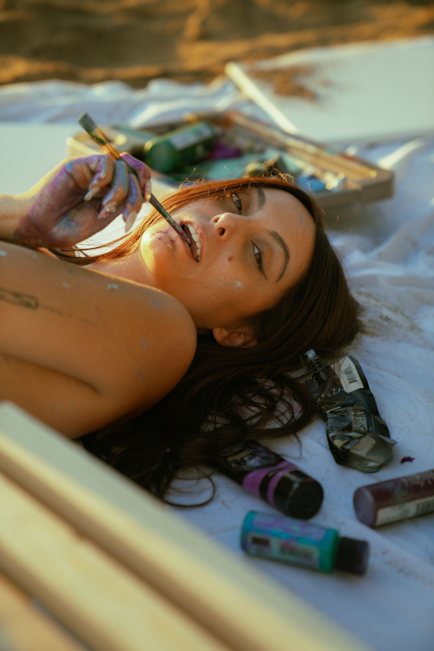 Close-up beach portraits with warm sunset lighting and scattered items on white blanket.