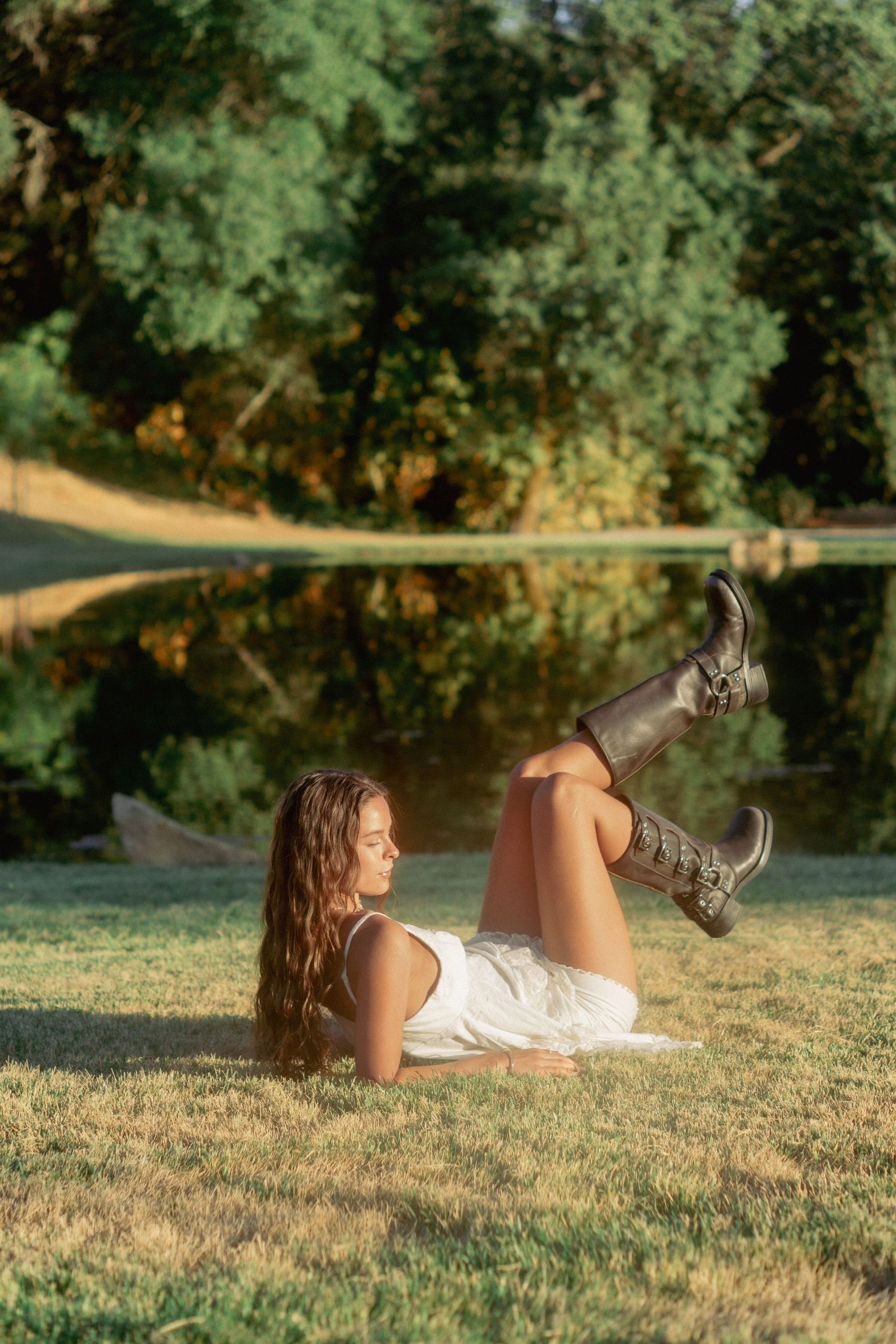 Person in white dress and boots lying on grass in a natural outdoor setting.