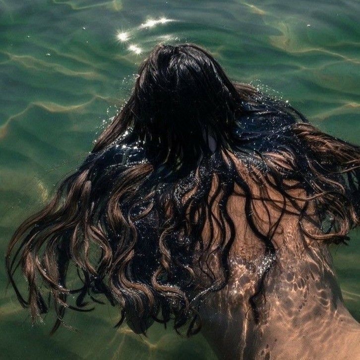 Dark wet hair floating in emerald green water with sunlight reflections.