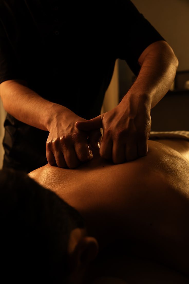 Therapist performing deep tissue back massage on client in dimly lit spa setting.