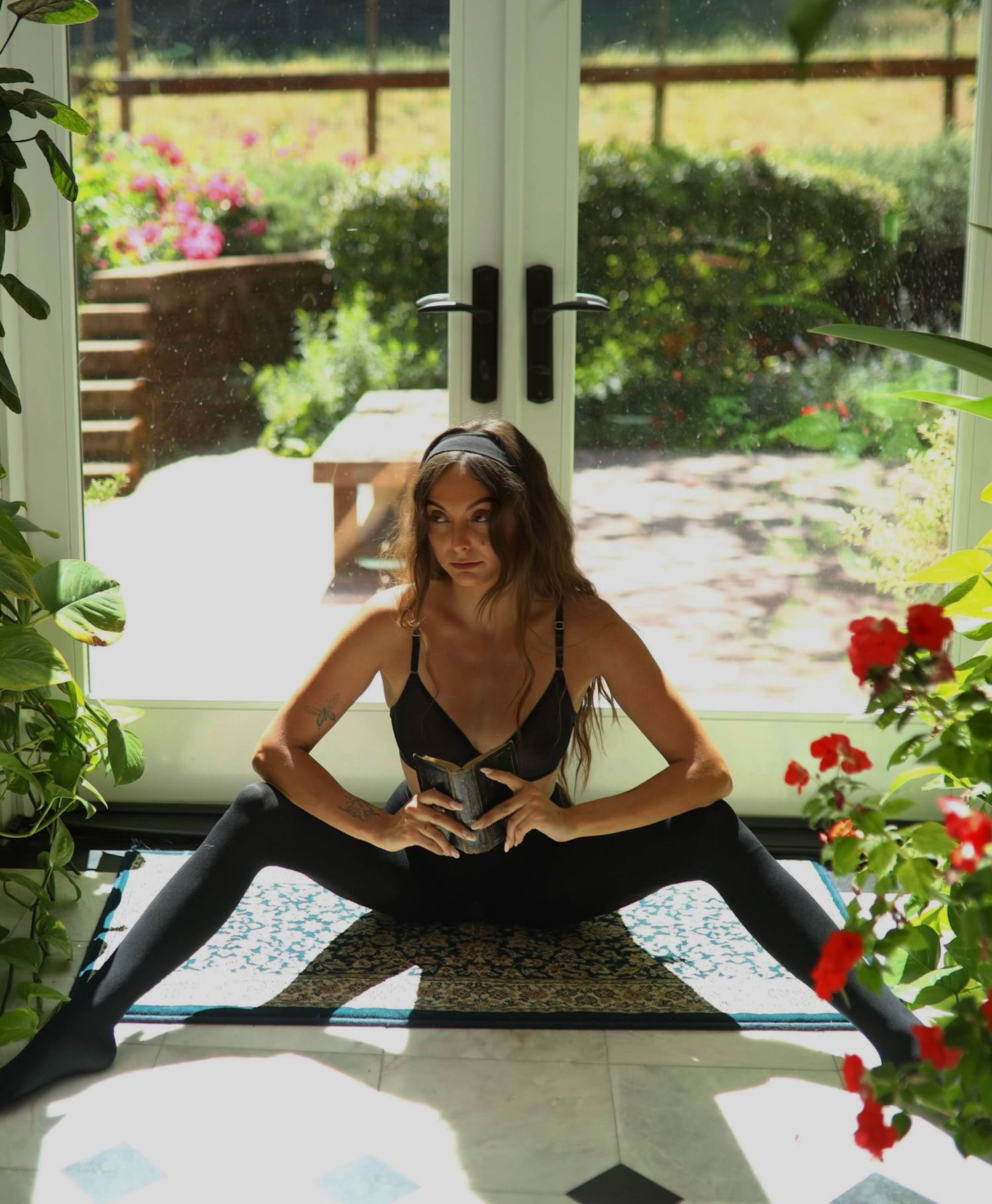 Person stretches in yoga pose by sunny window with red flowers.
