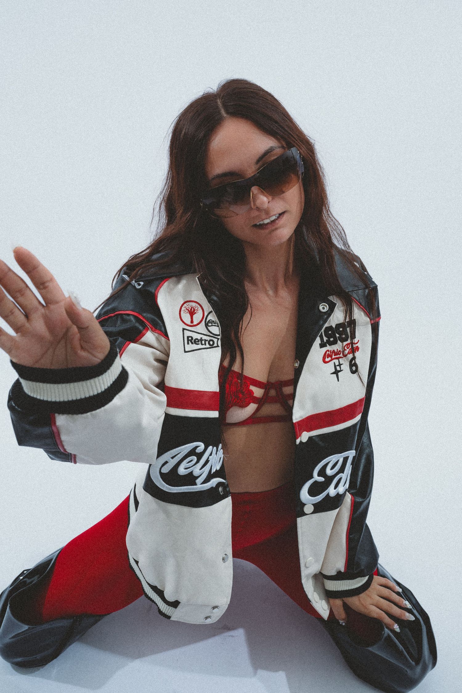 Person wearing red and white sports jacket poses playfully against white background.