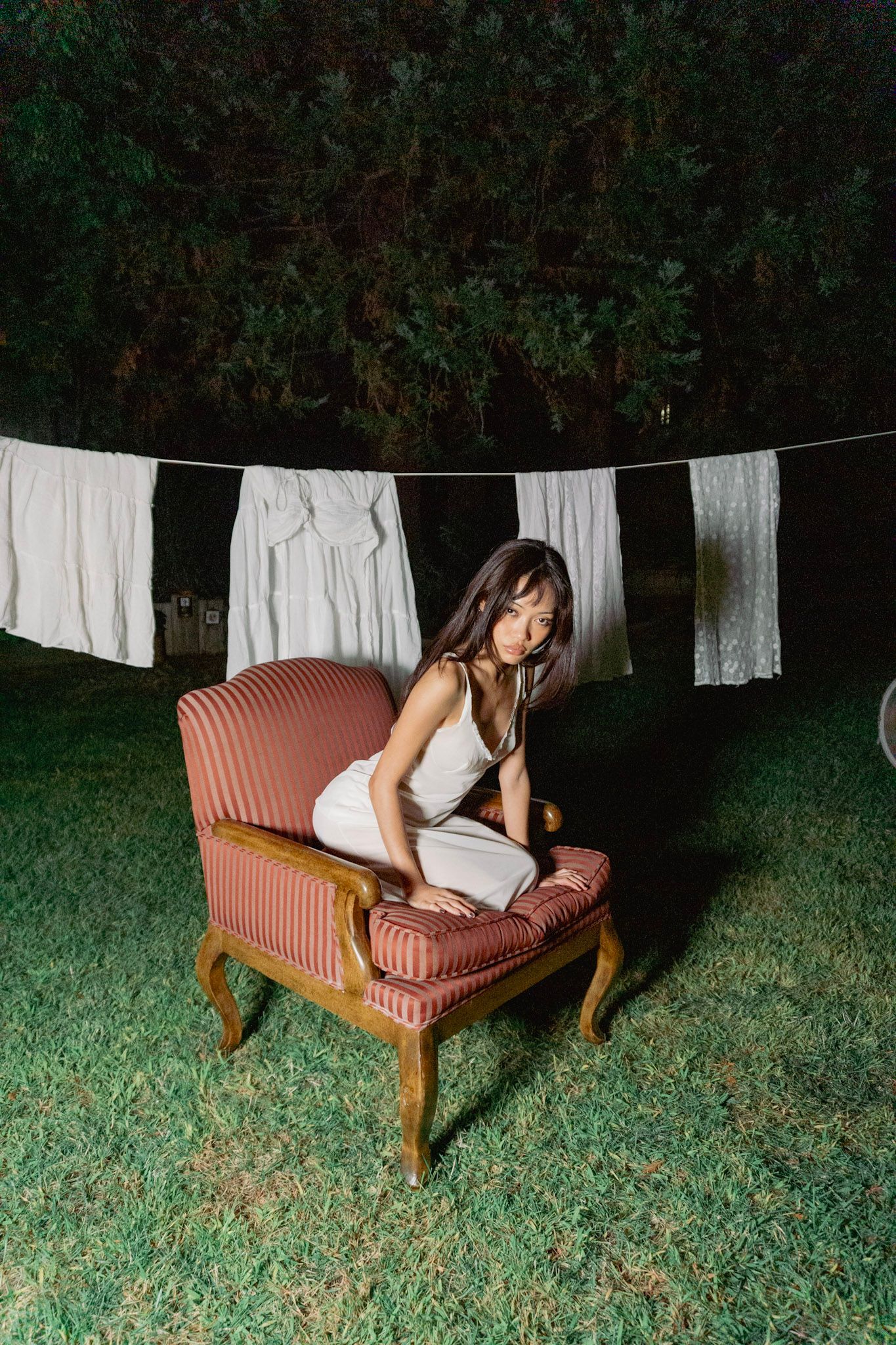 Nighttime photos of a person on a vintage pink striped chair with white laundry hanging on clothesline.