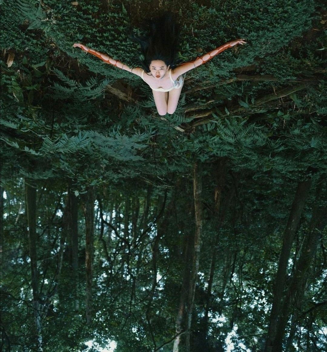 Figure emerging from lush green forest with arms spread wide in swimming motion.