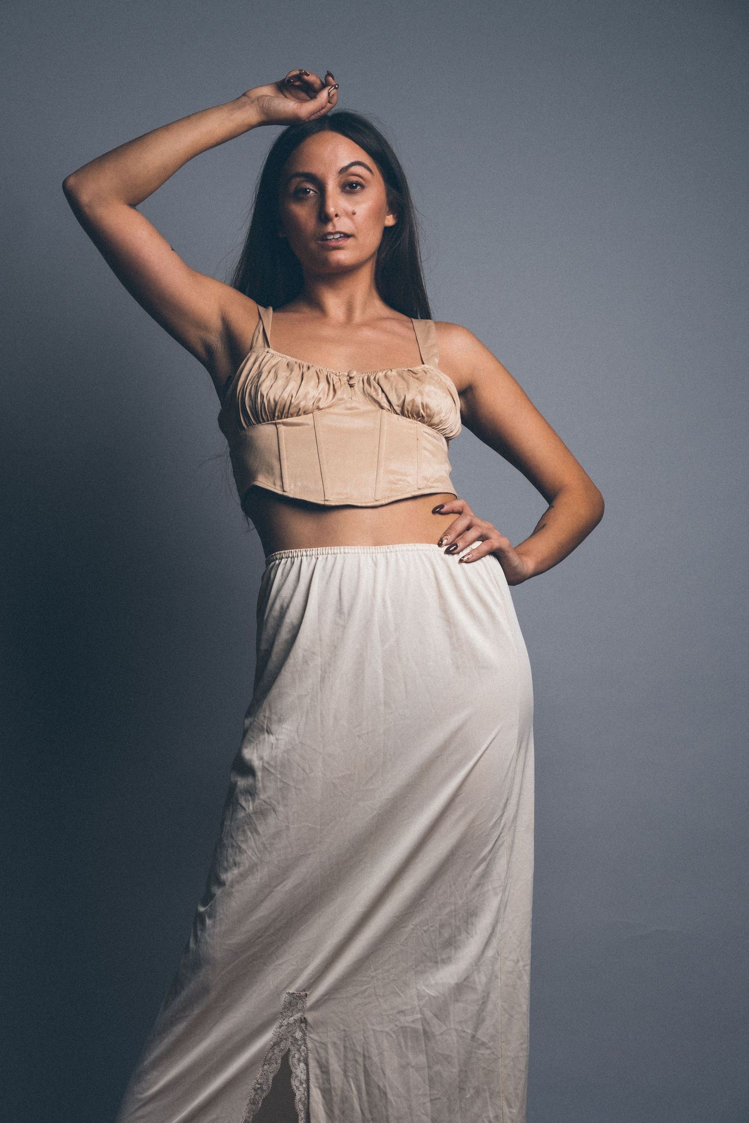 Model wearing cream colored dress poses elegantly in studio setting.