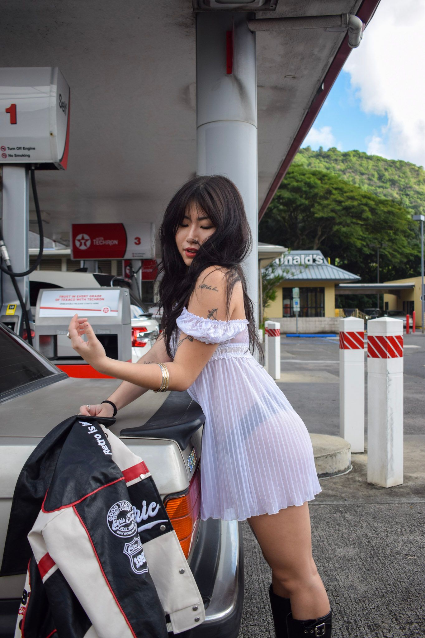 Person in white dress posing at a gas station with motorcycle.