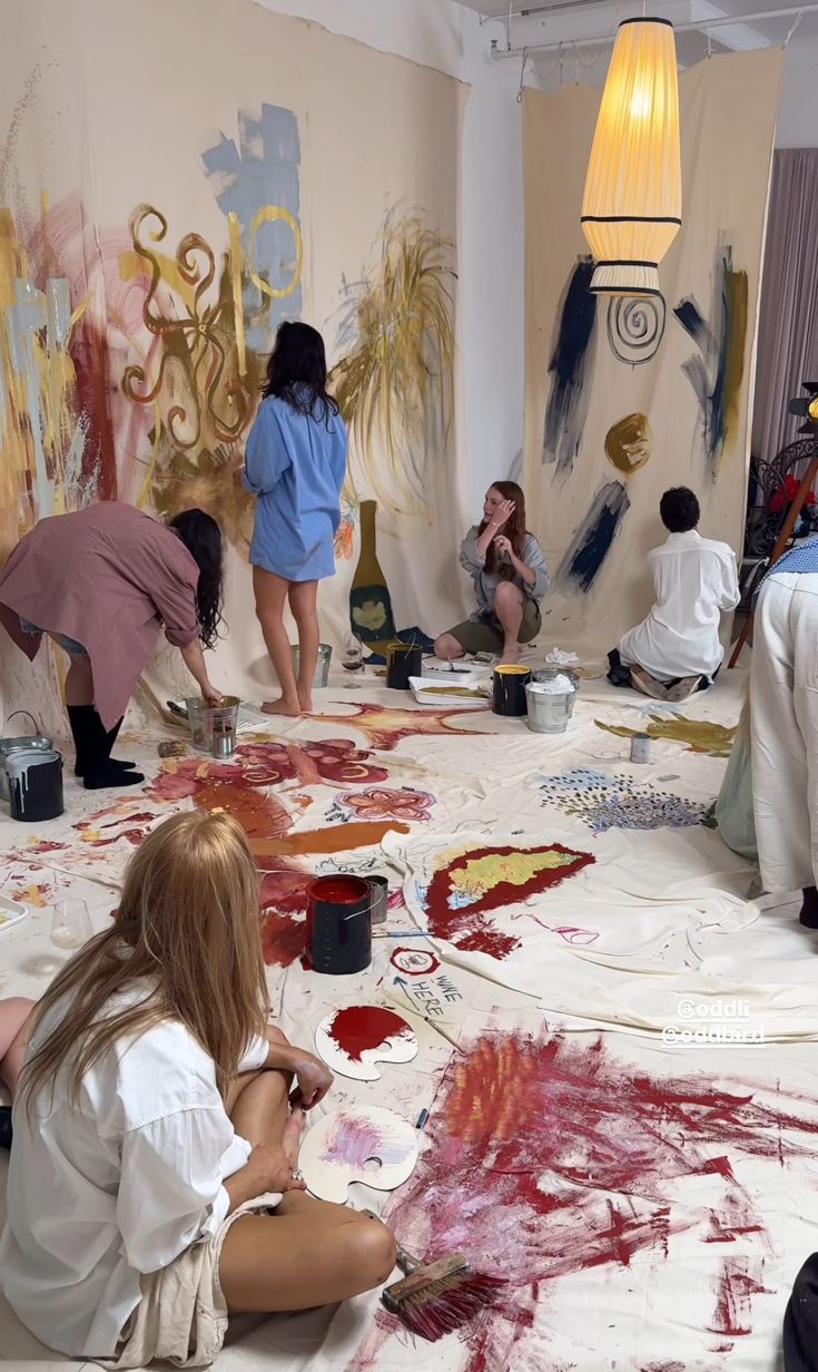 Artists collaboratively painting a large mural with colorful paints on a white wall.
