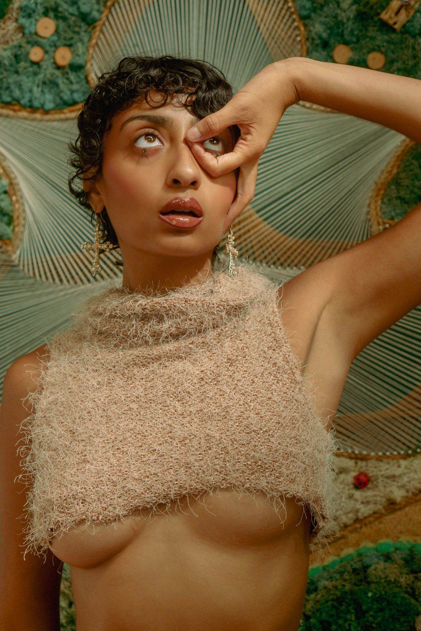 Artistic portrait against green backdrop with fuzzy beige crop top and dramatic lighting.