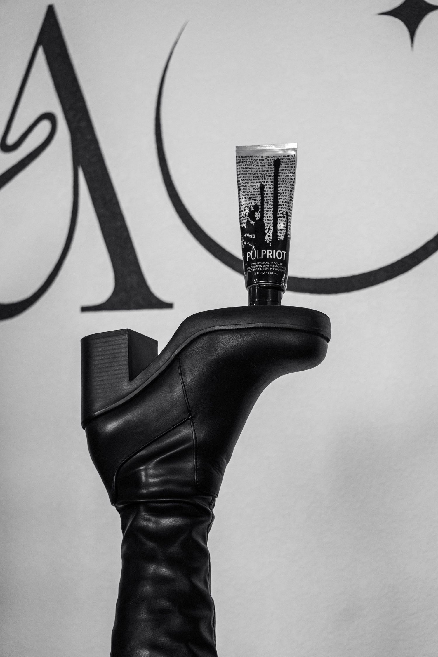 Black leather boots displayed with a bottle on top against a white background.