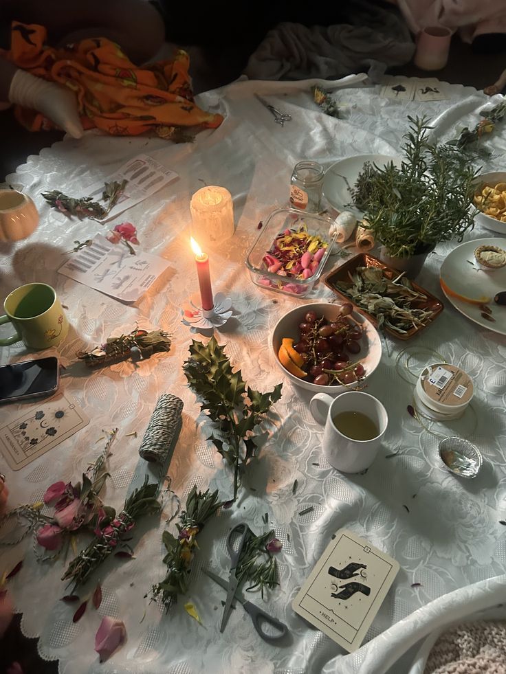 Witchy altar table with candles, dried herbs, flowers, tarot cards, and botanical arrangements on white cloth.