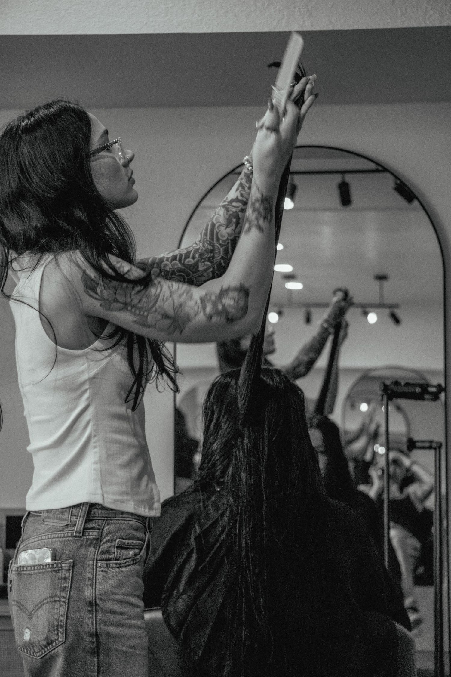 Hairstylist working on client's long dark hair in a modern salon setting.