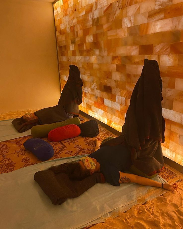 People in child's pose yoga position on mats in a warm salt cave room with glowing Himalayan salt brick walls.