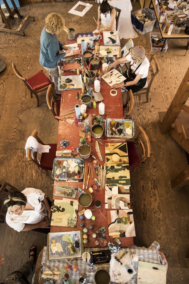 Overhead view of an artist's workspace with painting supplies and materials scattered on tables.