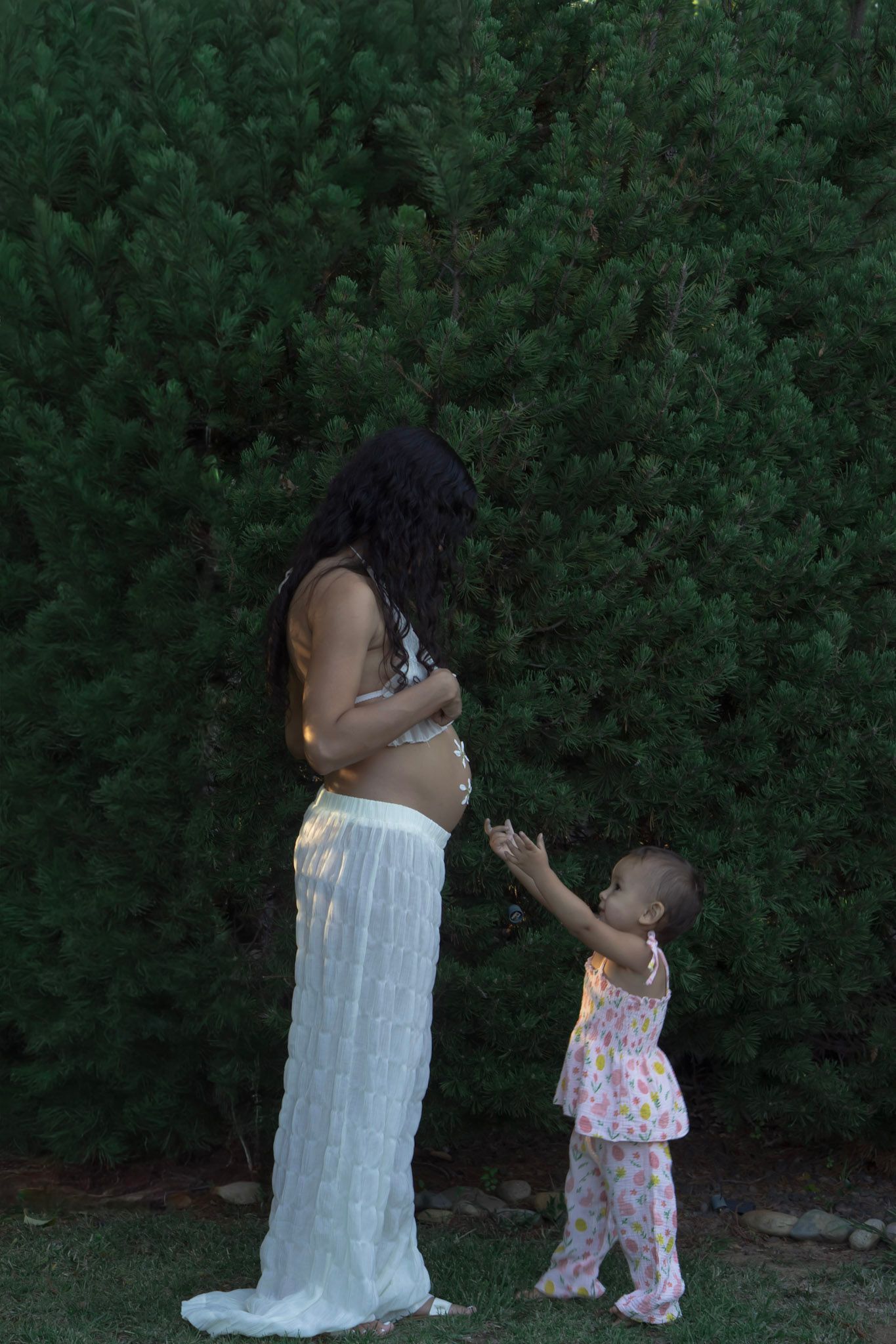 Person in white dress standing near small child outdoors.