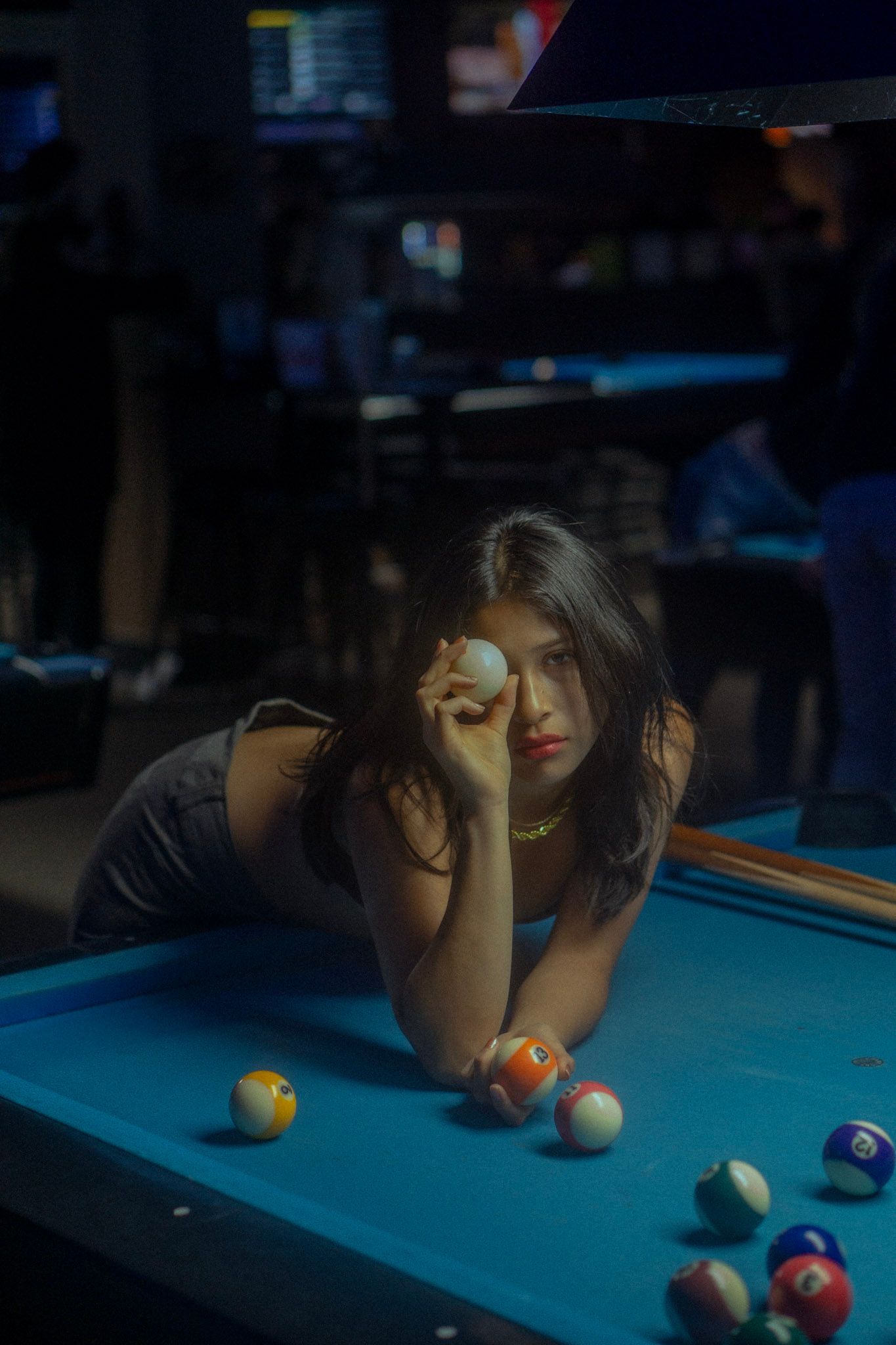 Player leaning over blue pool table examining billiard balls in dark lighting.