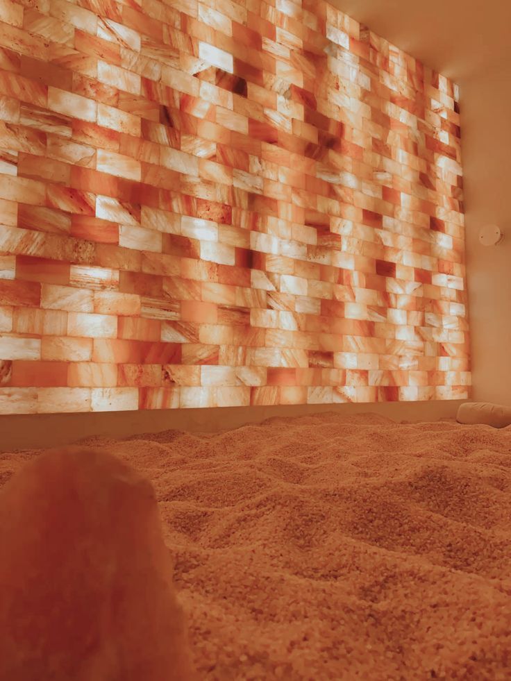 Himalayan salt therapy room with glowing pink salt brick wall and sandy salt floor for relaxation.