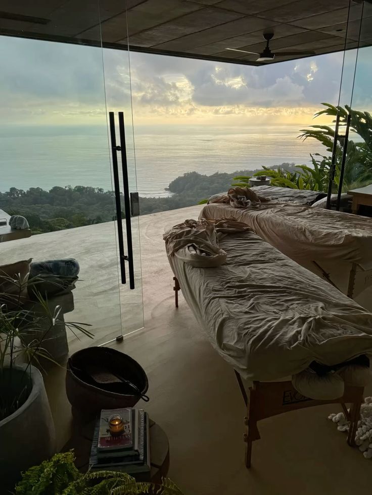Luxury open-air spa with two massage tables overlooking a stunning ocean sunset, surrounded by lush tropical greenery.