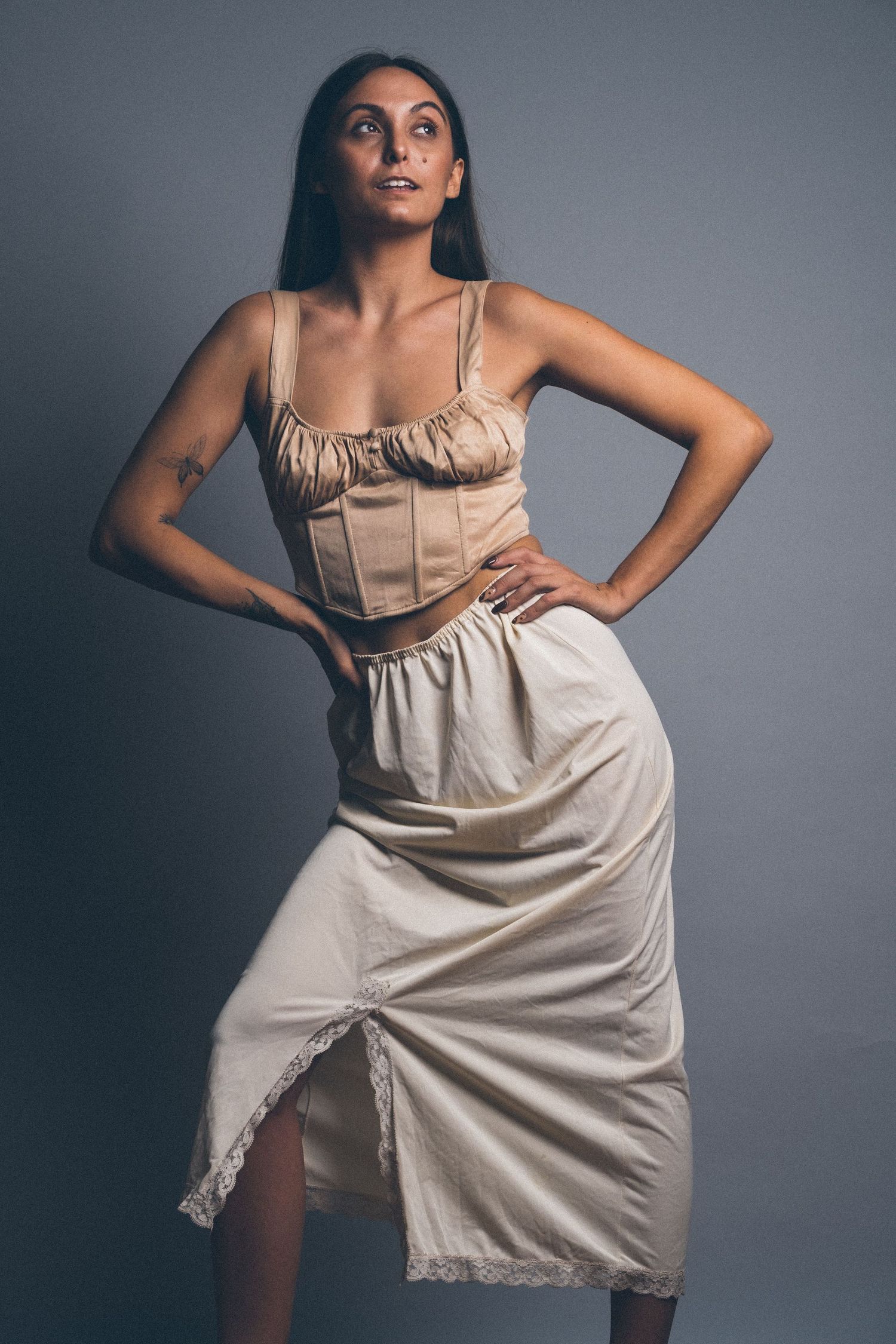 Fashion portrait of woman in beige corset dress against gray studio backdrop.