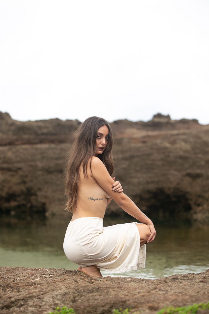 Woman in white dress poses elegantly by coastal waters.