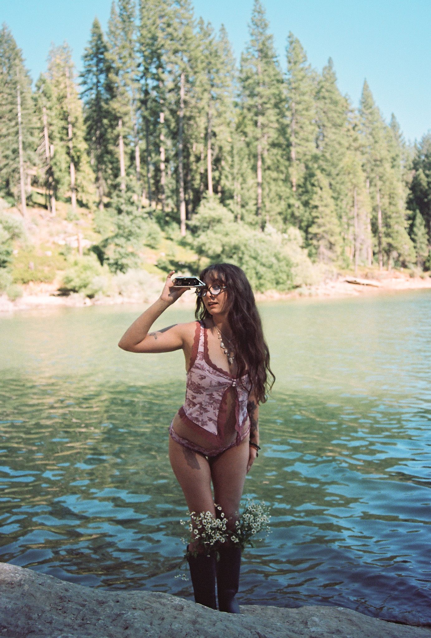 Summer lake photoshoot with pine trees and clear blue water in background.