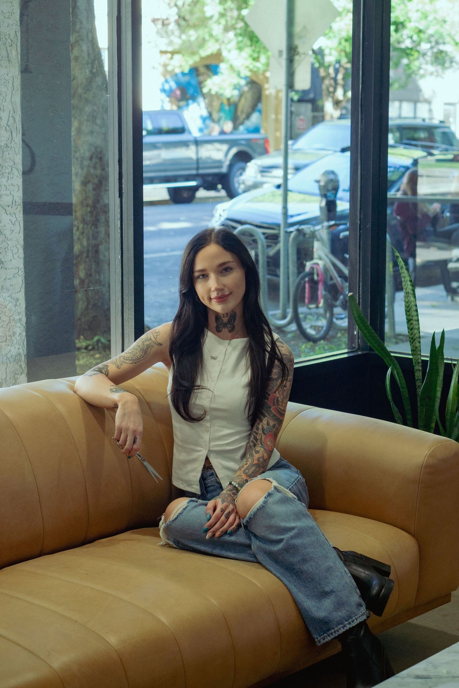 Person in casual attire lounging on a tan couch near large windows.