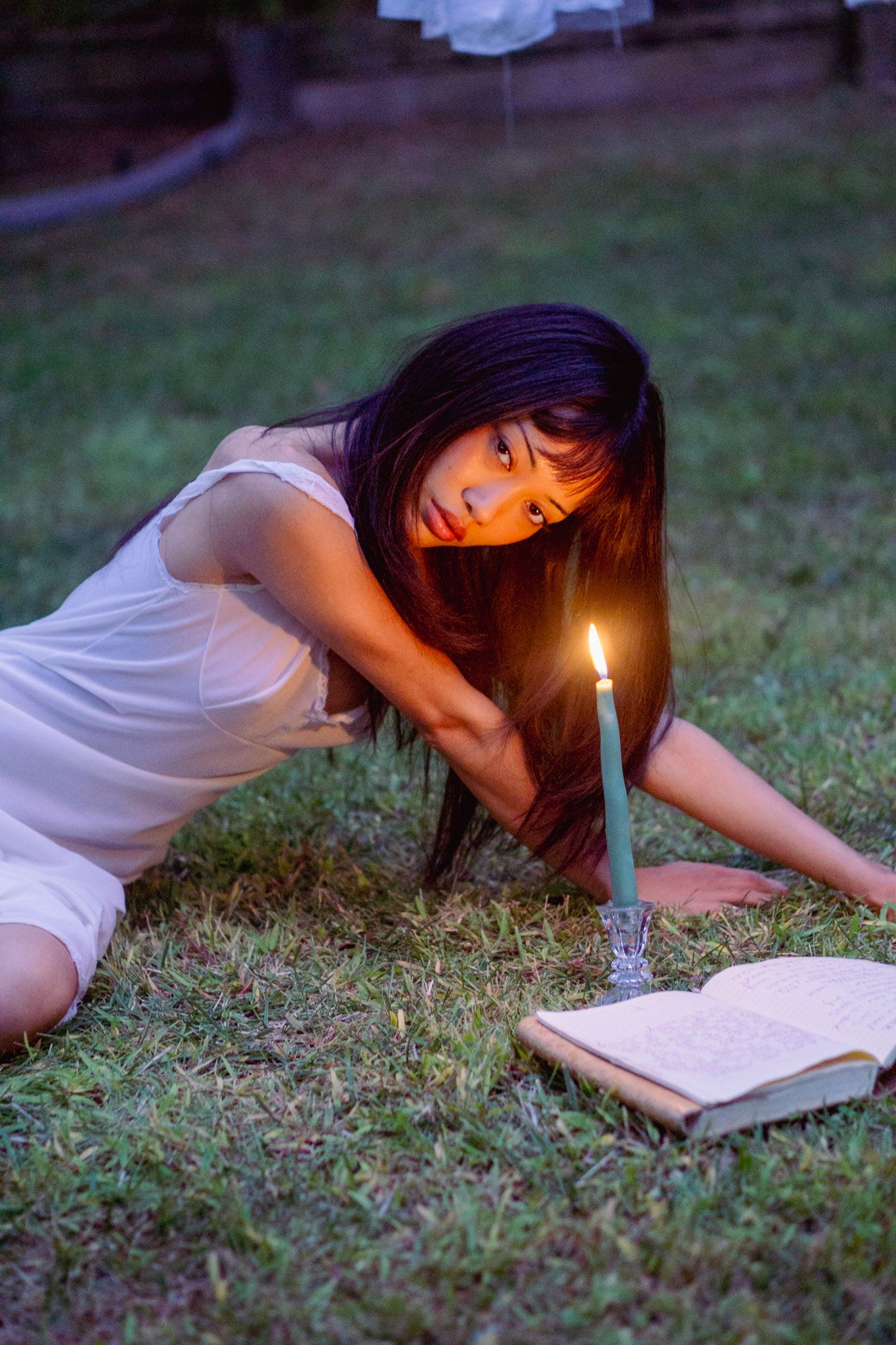 Person reading book by candlelight on grass at twilight.