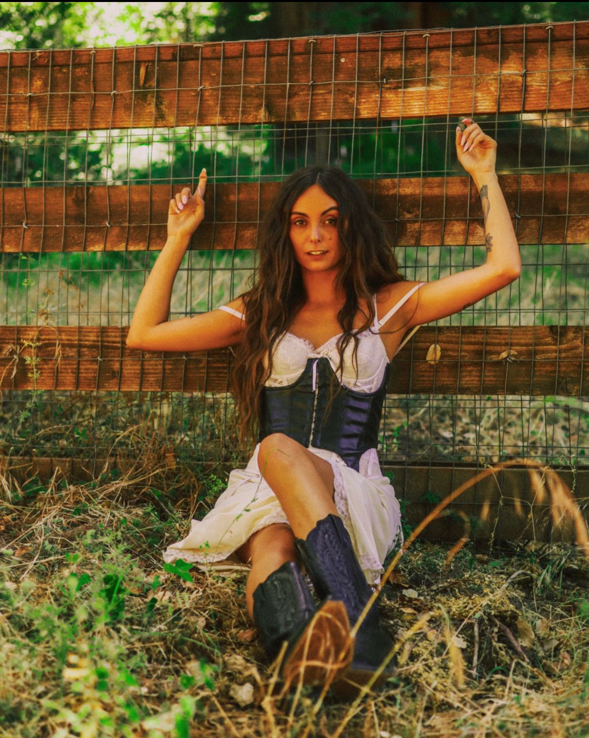 Artistic outdoor photoshoot with white dress and rustic fence in summer garden setting.