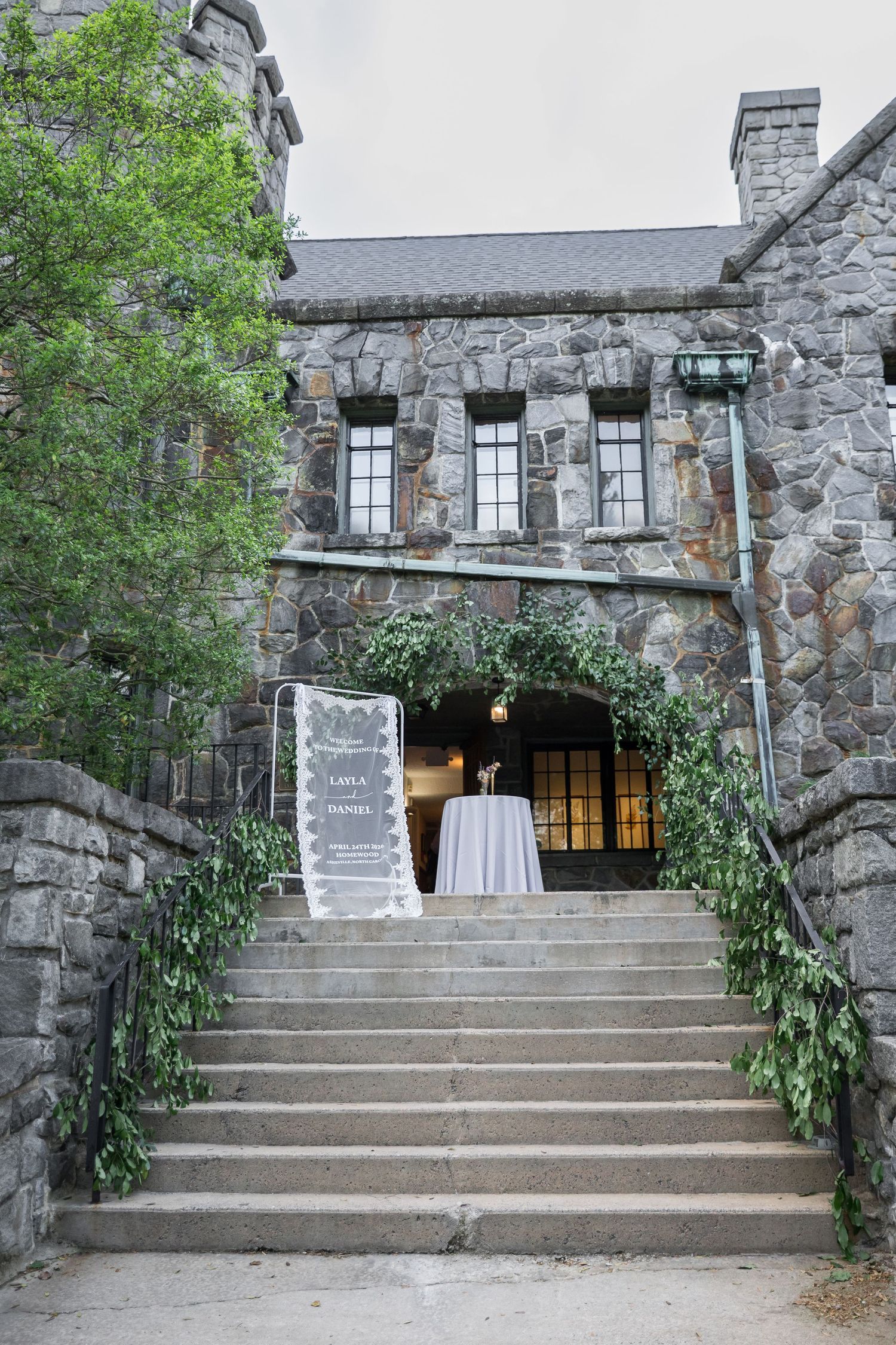 Stone castle wedding venue entrance with floral arch, greenery, and welcome sign at top of stone steps.