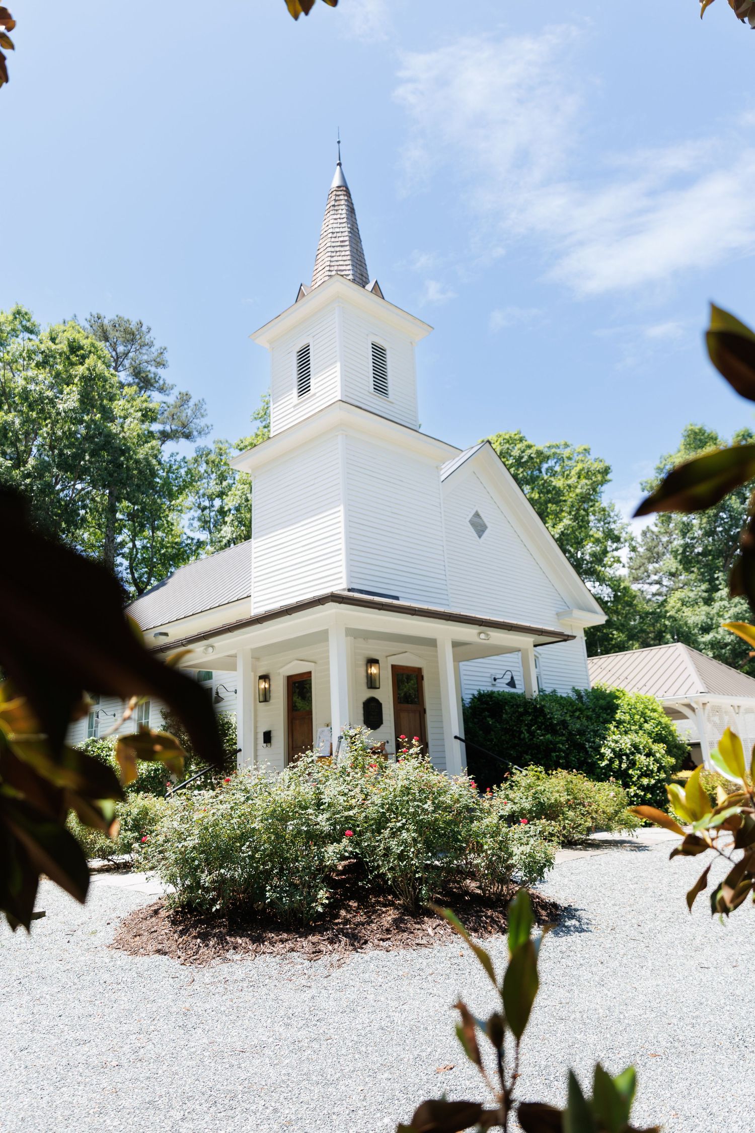White church wedding venue with steeple framed by green leaves and blue sky.