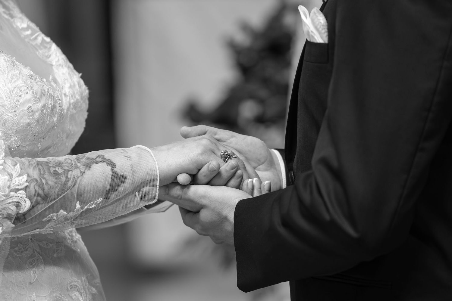 Black and white close-up of bride placing wedding ring on grooms hand during ceremony.