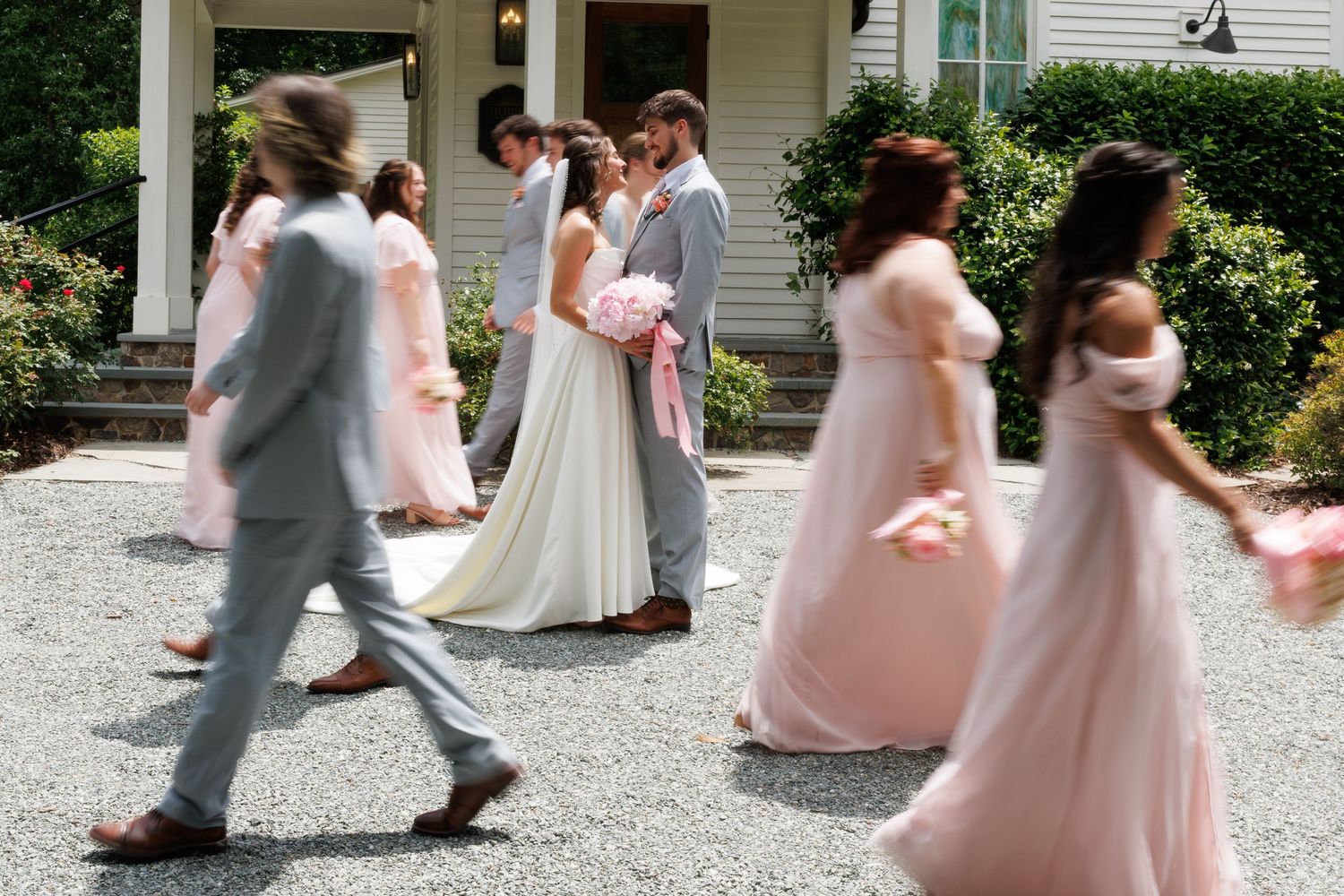 Wedding party in motion with bride and groom at center, bridesmaids in blush pink gowns and groomsmen in gray.