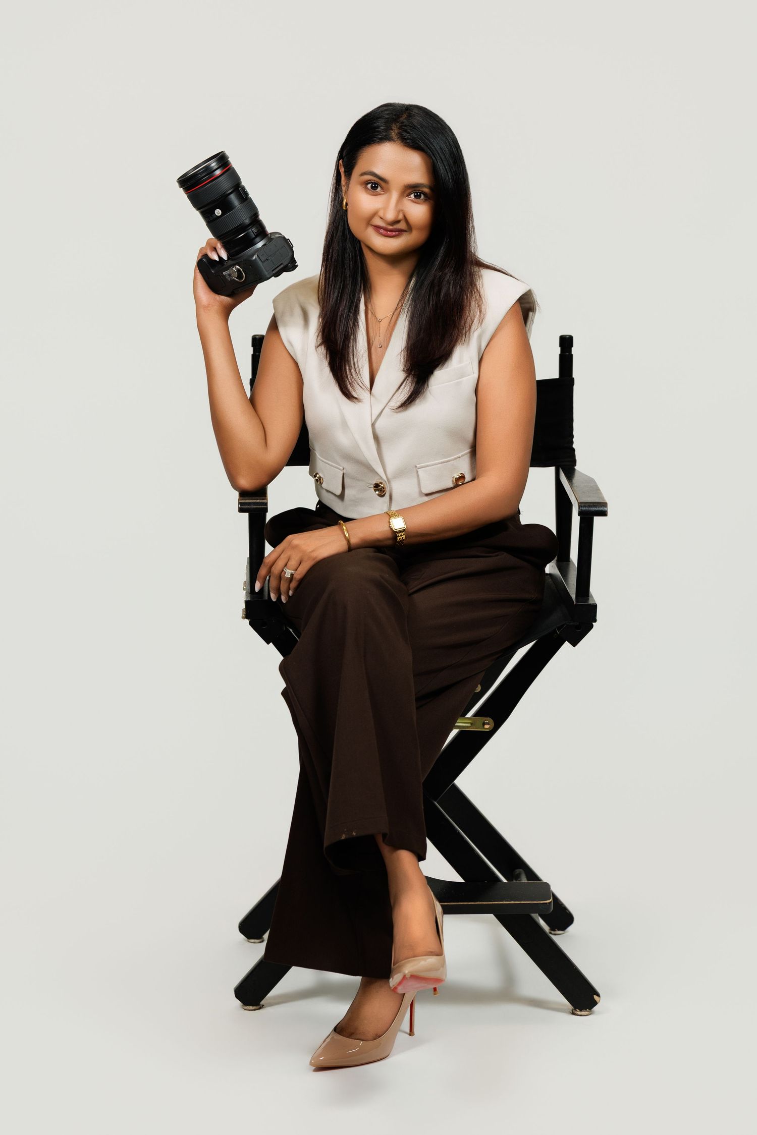 Professional female photographer sitting in director's chair holding a DSLR camera in a studio setting.