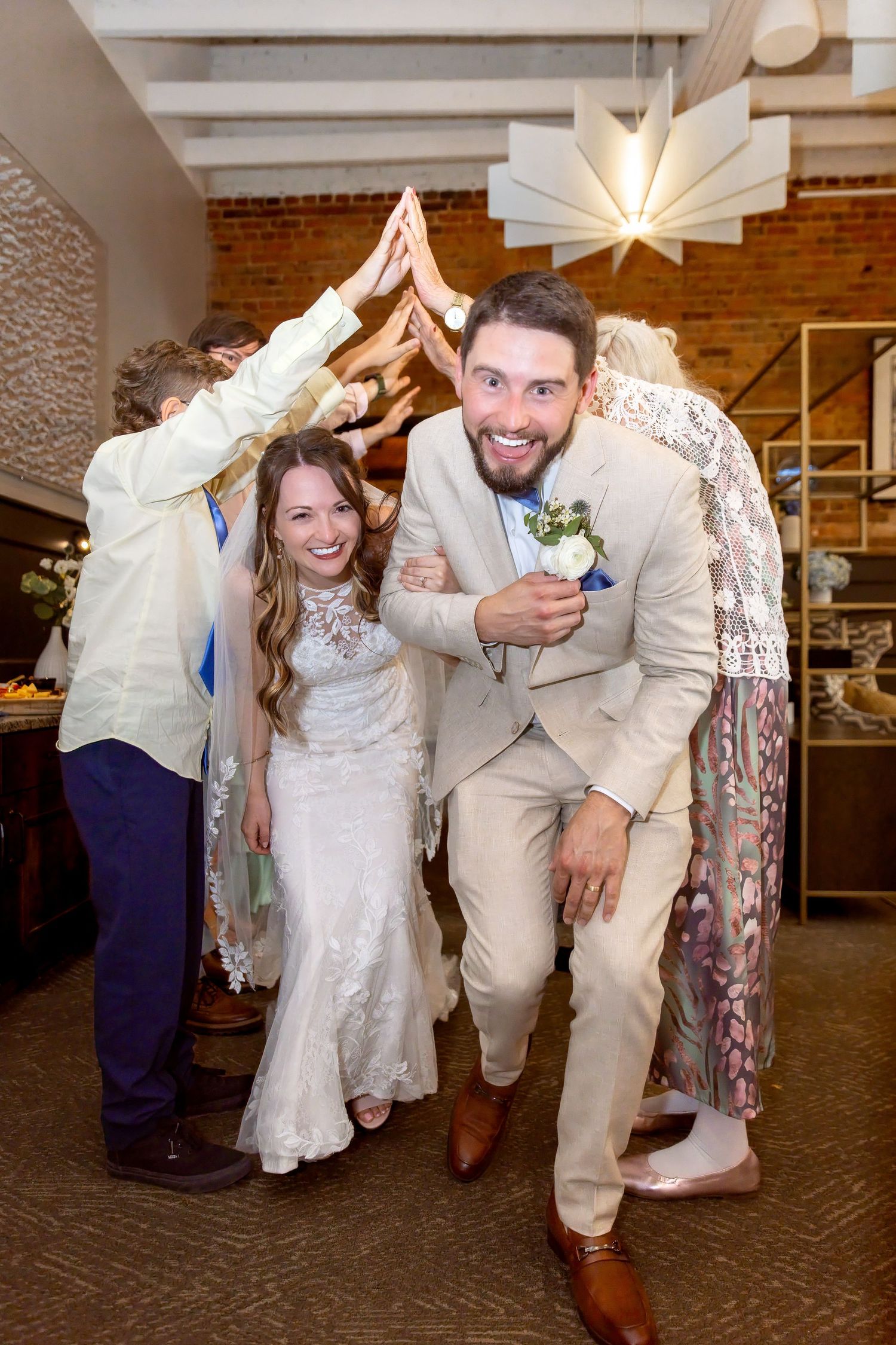 Bride and groom laughing as they duck under an arch of hands during their wedding reception entrance.