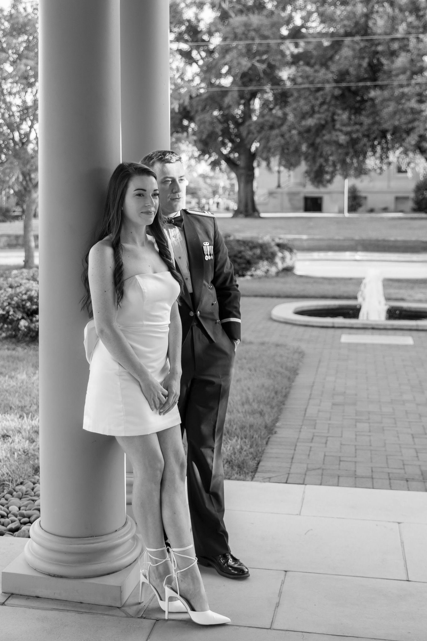 Black and white photo of a couple posing by a column, groom in military dress uniform.