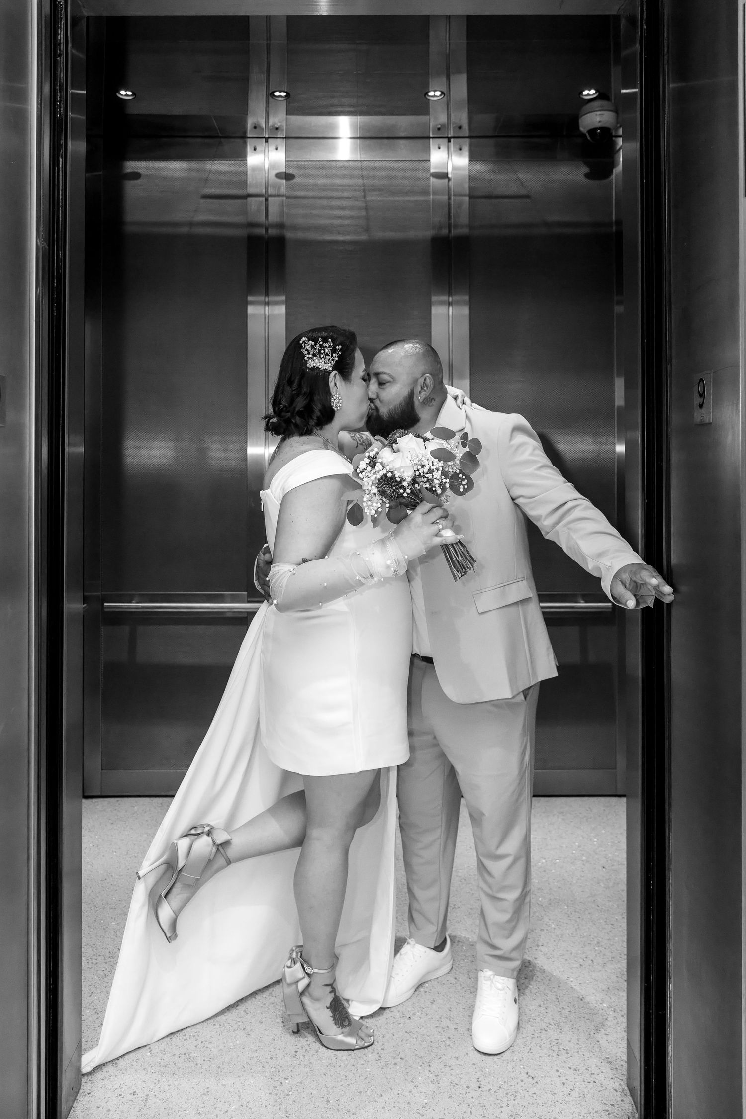 Black and white photo of a bride and groom sharing a kiss in an elevator, bride holding a bouquet.Wake country courthouse