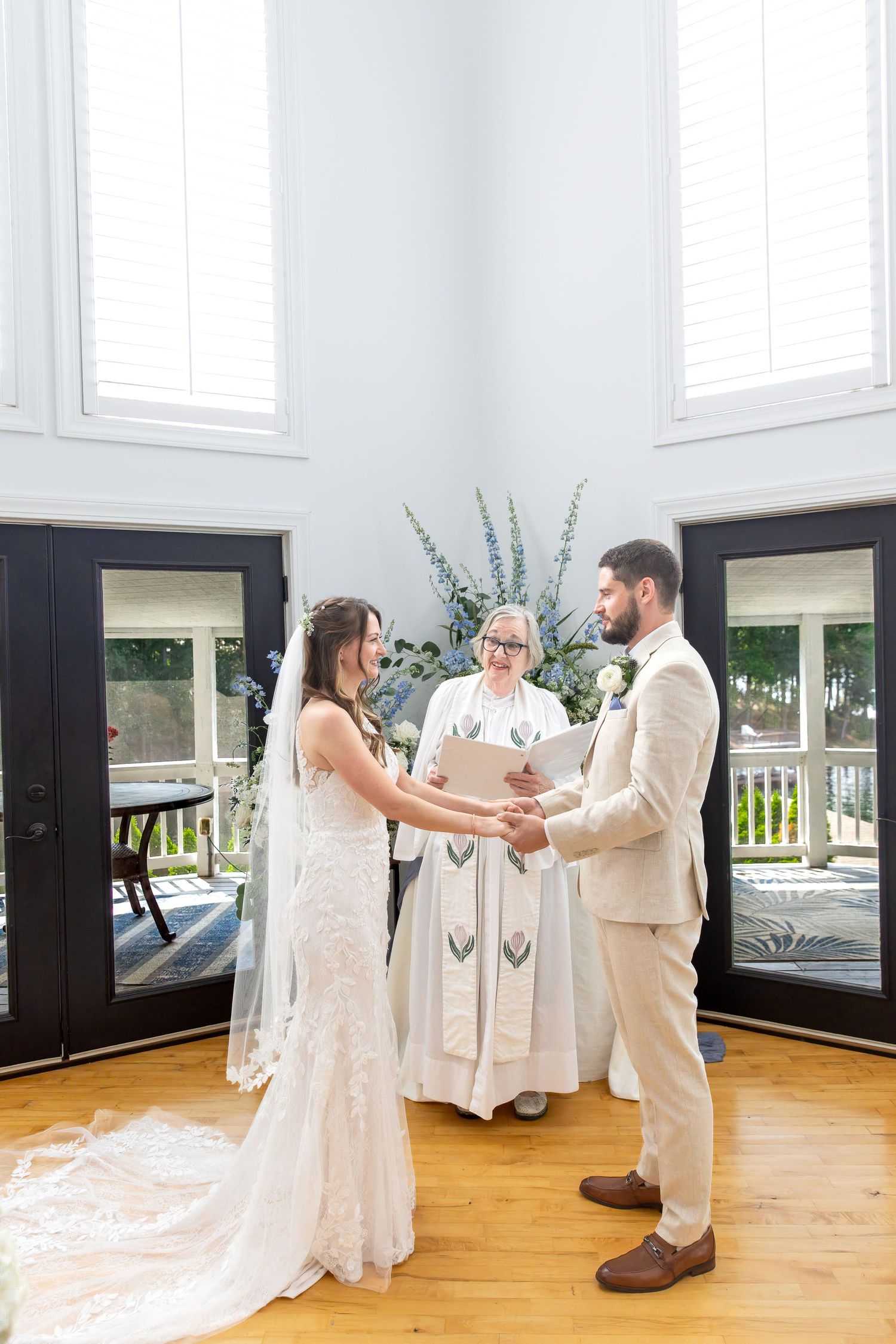 Bride and groom exchanging vows while holding hands before an officiant in a bright indoor ceremony.